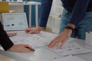 Close up of analysis documents with data charts on desk. Business people using papers and digital tablet for marketing strategy with project presentation. Colleagues planning design
